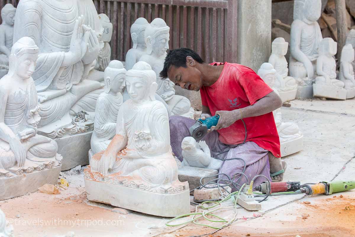 A man carving marble statues of Buddha with an angle grinder